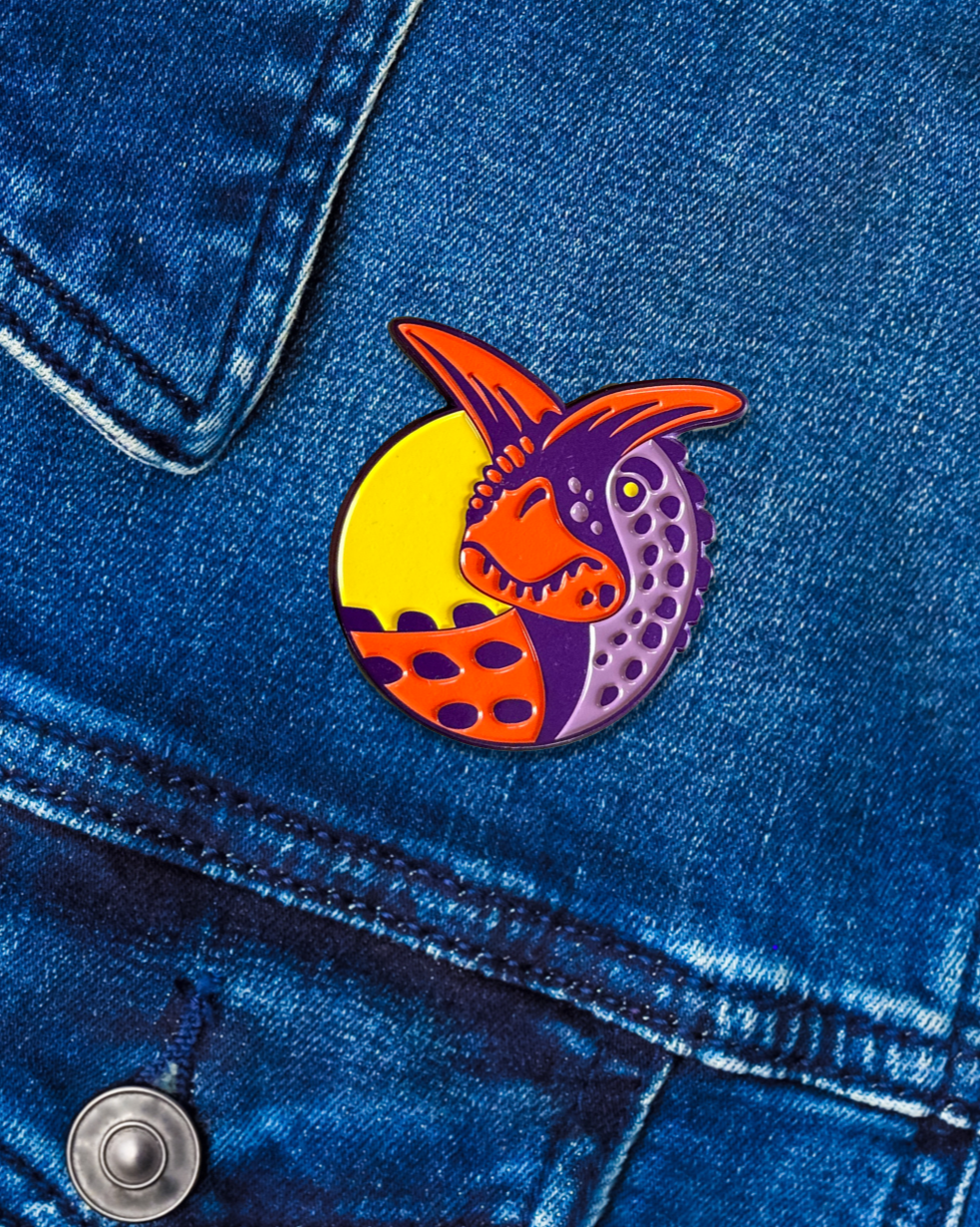 A colorful Carnotaurus enamel pin attached to a denim fabric.